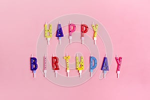 Colored candles on cake in the form of letters happy birthday, gift boxes on pink background