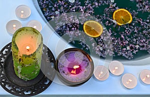 Colored candles on the edge of the bathtub full with blue water and lilacs