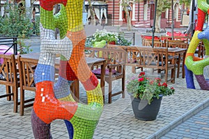 Colored ceramic mosaic decoration on a gray sidewalk in front of wooden brown chairs and a table on an open summer veranda