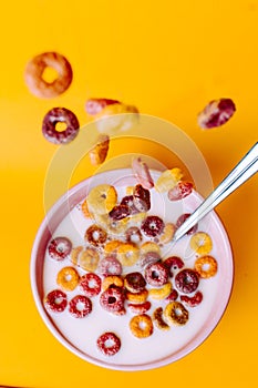 Colored cereals falling in a pink bowl with milk