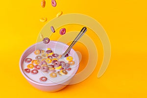 Colored cereals falling in a pink bowl with milk and a spoon