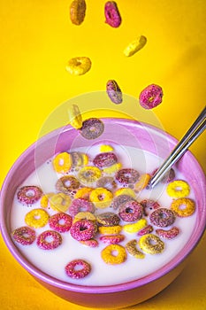 Colored cereals falling in a pink bowl with milk and a spoon