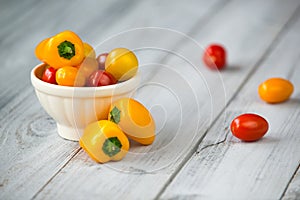 Colored cherry tomatoes and mini paprika in a bowl on a wooden t