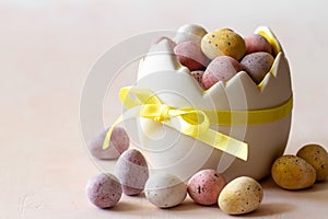 Colored chocolate easter eggs candy in eggshell shaped bowl on pink background, easter sweets, decoration