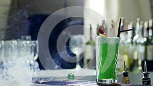 Colored cocktail with plastic straws and berries in glass stands on bar counter in fog