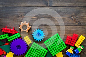 Colored construction toys for children mockup. Lego blocks, minifigures on dark wooden background top view copy space