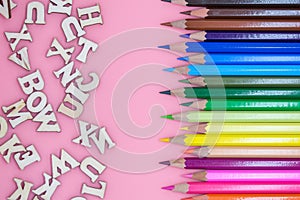 colored crayons and letters spread on pink background concept