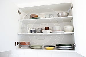 Colored dishes on shelves in an open white kitchen cabinet.
