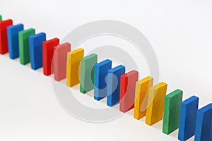 Colored dominoes stand in a row on a white background. A chain reaction dominoes photo