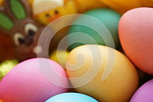 colored Easter eggs in basket with a chocolate Easter bunny and a chick in the background
