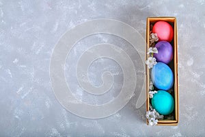 Colored Easter eggs in a gift box on a gray concrete background.