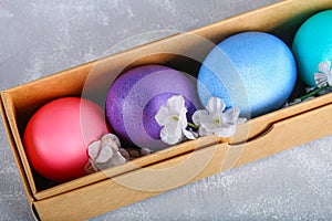 Colored Easter eggs in a gift box on a gray concrete background.