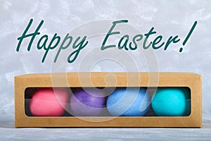 Colored Easter eggs in a gift box on a gray concrete background.