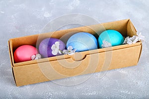 Colored Easter eggs in a gift box on a gray concrete background.