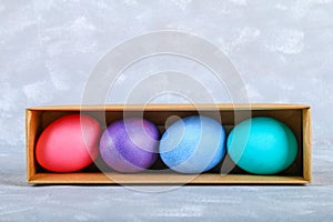 Colored Easter eggs in a gift box on a gray concrete background.