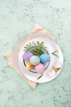 Colored easter eggs and green leaves on a round white plate on a photo