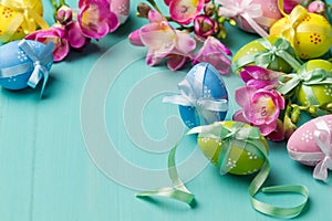 Colored Easter eggs with ribbons and flowers on a turquoise table