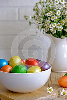 Colored Easter eggs with wild chamomy on old wood table on brick wall background