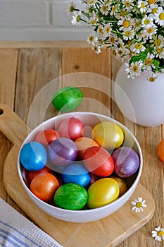 Colored Easter eggs with wild chamomy on old wood table on brick wall background