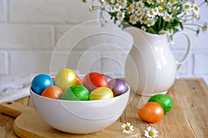 Colored Easter eggs with wild chamomy on old wood table on brick wall background