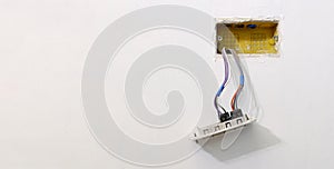 Colored electrical cables coming out of a corrugated tube of an electrical box, from a white wall, in an apartment under