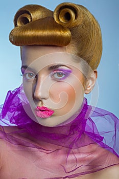 Colored fashion beauty woman with pink tulle and candy colored pearls on her lips and fantasy golden hairstyle on blue background.