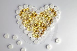 Colored heart pills and capsules arranged in a heart shape on a white background, cardiovascular medication concept.