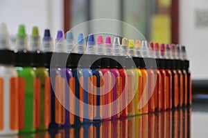 Colored inks in plastic containers formed in a row and background bokeh