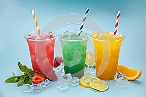 Colored lemonades in plastic cups with ice, fruits and berries photo