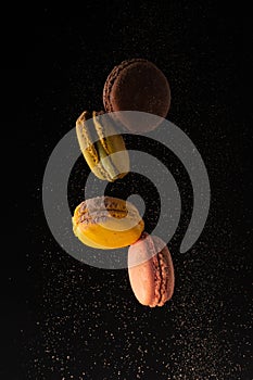 Colored macaroons, French cookies, colored levitates with cocoa powder on a black background