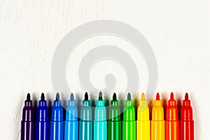 Colored markers without caps lie on a white wooden table