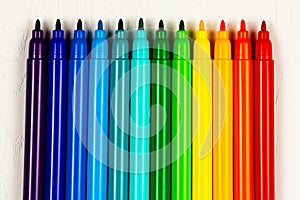 colored markers without caps lie on a white wooden table