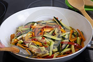 Colored mix of filleted fresh vegetables, courgettes, carrots, peppers and eggplants sautÃ©ed in a pan to be used for rolls