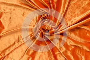 Colored orange textile satin fabric folded in folds and waves with highlights and texture