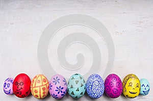 Colored ornamental eggs for Easter with painted faces border ,place for text wooden rustic background top view close up