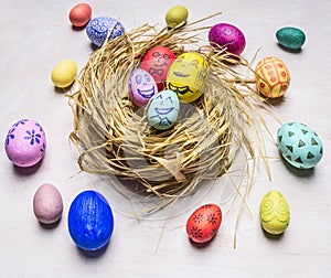 Colored ornamental eggs for Easter with painted faces lie in a nest wooden rustic background top view close up