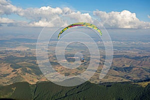 colored Paraglider flying over mountain valley on a sunny clear day