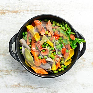 Colored pasta with peas and vegetables in a black bowl. Top view.