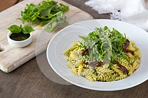 Colored pasta with rukola and basil on white plate with sauce.