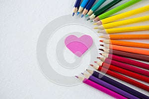 Colored pencils arranged in semi circle with heart on white background