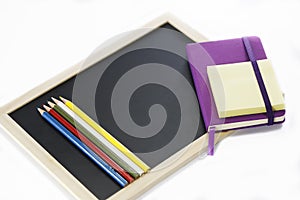 Colored pencils, black board, notebook and memopad photo