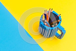 Colored pencils in a bucket on blue and yellow background. Back to scool concept photo