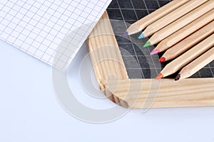 Colored pencils, chalk blackboard and a paper block paper sheet isolated on white background