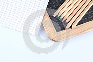 Colored pencils, chalk blackboard and a paper block paper sheet isolated on white background