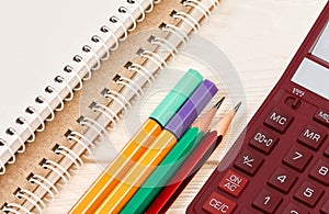 Colored pencils, desktop calculator and notebooks on white wooden table.  School and office supplies. Top view