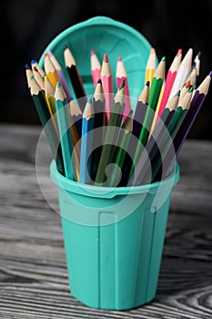Colored pencils for drawing.  They stand in a pencil holder in the form of a trash can. On pine boards