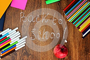 Colored pencils, felt-tip pens and markers, notebooks, stickers a red apple on the wooden background with the back to