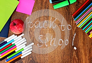 Colored pencils, felt-tip pens and markers, notebooks, stickers a red apple on the wooden background with the back to school insc