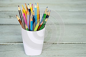 Colored pencils in a glass on a wooden background