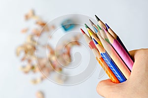 Coloured pencils in hand against blurred shavings on white backgr